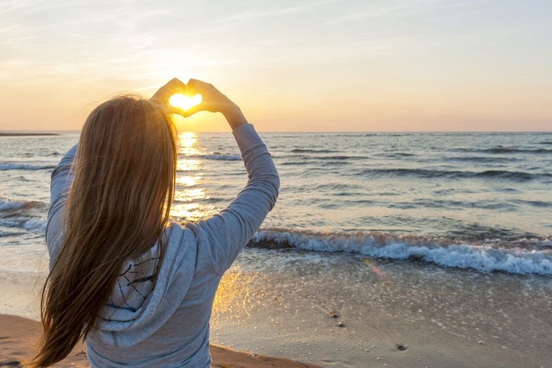 Woman on beach making heart shape with hands